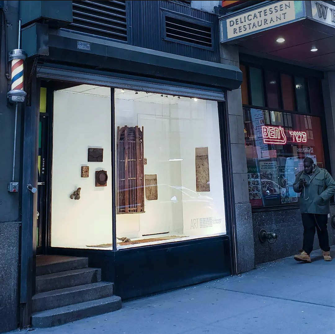 A storefront window featuring wooden art pieces hung on the walls, next door to a Ben's Deli.