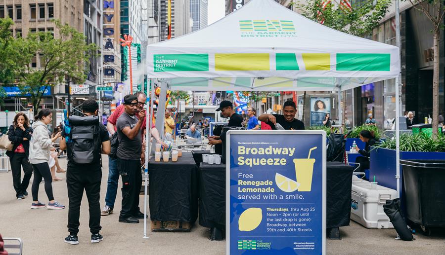 Free lemonade being handed to a line of people from under a tent on a public plaza