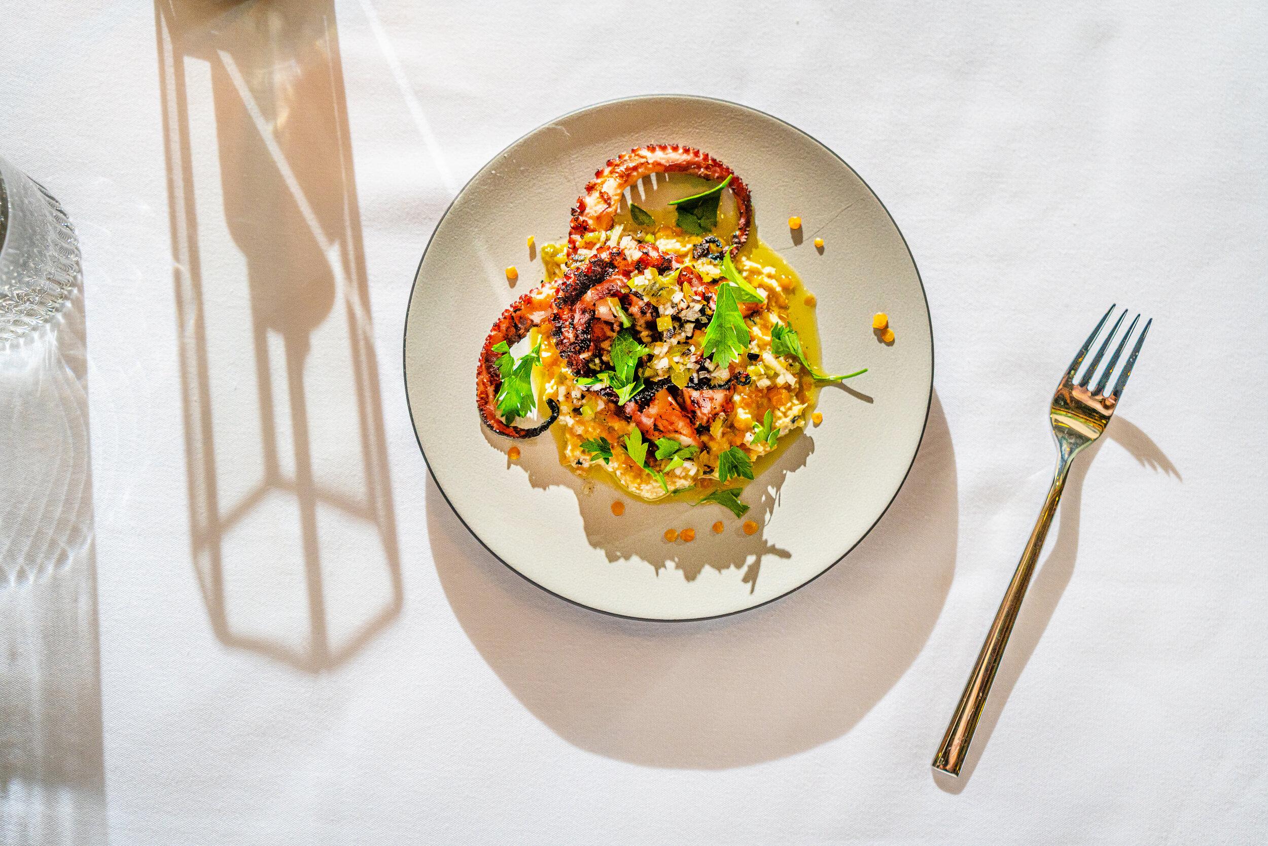 An artfully plated octopus dish on a white plate on a white tablecloth. 