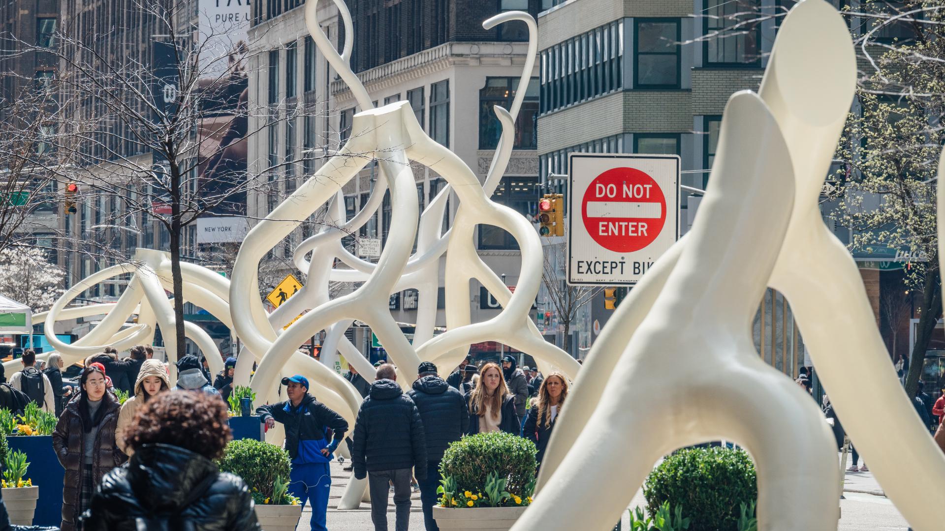 A Wide view of multiple of the white steel sculptures that bend and turn like smooth roots as people walk by