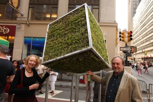 Moss-covered cube sculpture flanked by the two artists who created it