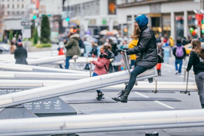 Daytime view of a row of over-sized seesaws with people atop them.