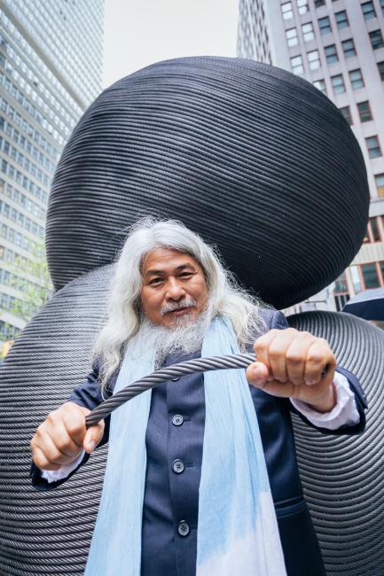 The artist standing in front of one of his sculptures, holding a length of cable