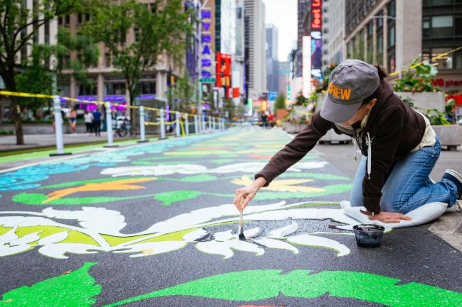 Close-up of artist kneeling on street mural and painting a section. 