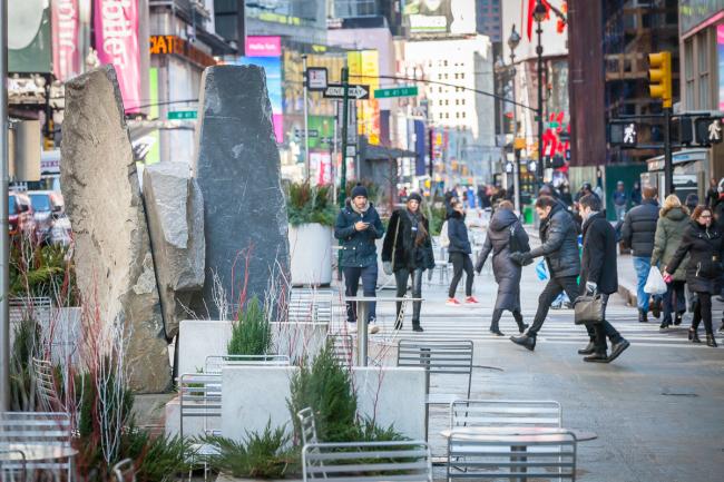 Large stone sculpture with table and chairs in foreground and pedestrians behind