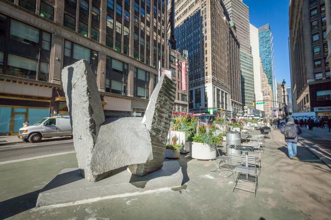 Stone sculpture installed on plaza with table and chairs nearby