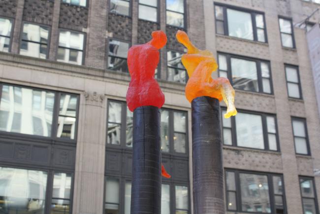 A pair of figures, one red and one yellow, each atop a black post
