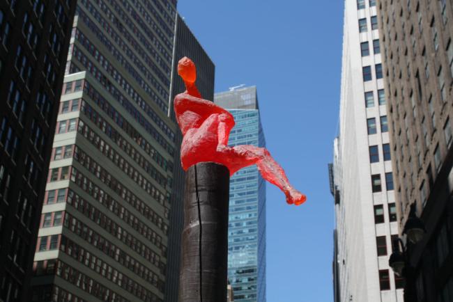 Red figure atop a black post with skyscrapers in the background