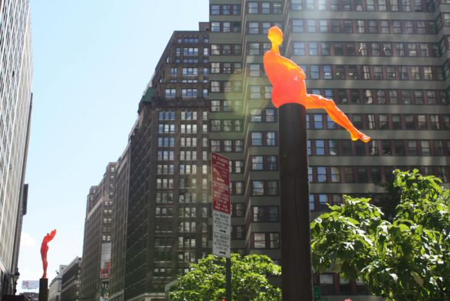 Sculpture of an orange human figure atop a black post.
