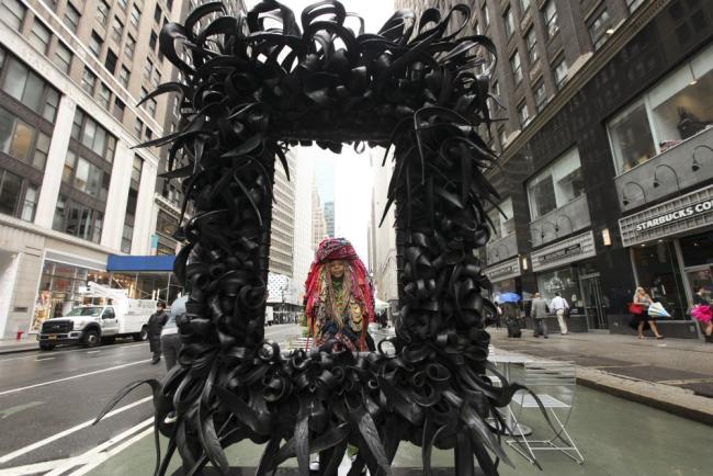 Sculpture made from recycled materials frames the artist who is standing behind it.