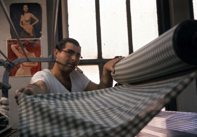 Man with a cigar pulling a length of fabric from a roll.