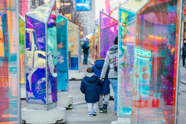 A woman and two children walking between two rows of glass prism sculptures