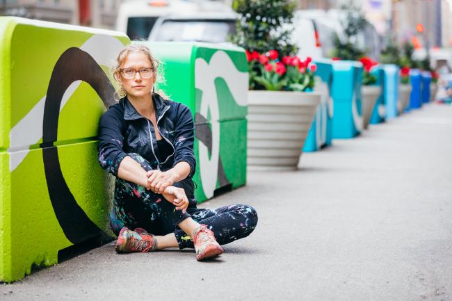 The artist seated on the ground in front of one of the green cubes that make up her mural.