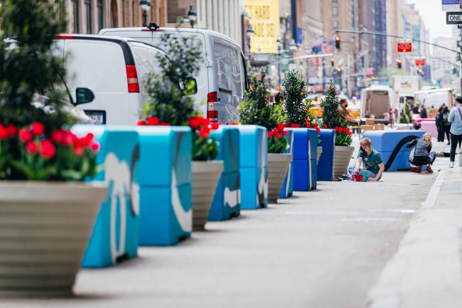 A row of cubes of varying shades of blue, set between planters along a sidewalk