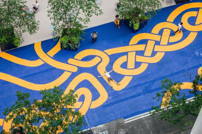 A shot from above of artist Steed Taylor laying down on his mural, arms and legs spread out like he is making a snow angel. 