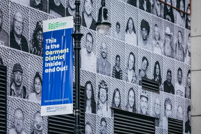 Another wall of faces of new yorkers, at an angle with a Garment District banner in the foreground. 