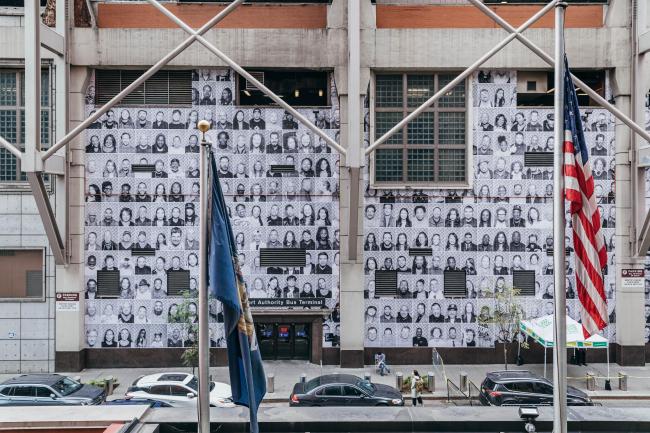 A wall of black and white photos of the faces of New Yorkers on the side of the Bus Terminal.