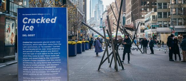 A sign in the foreground for CRACKED ICE. Behind it is a sculpture featuring a large boulder supported by diagonal metal poles