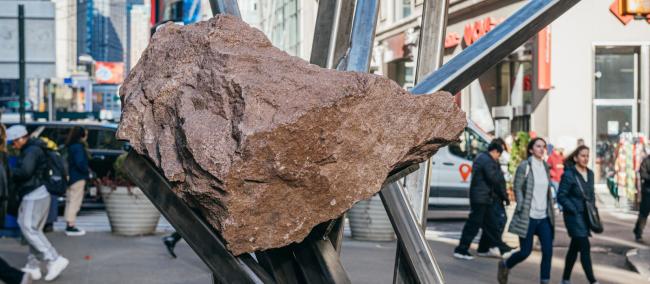 A large boulder supported by diagonal metal poles