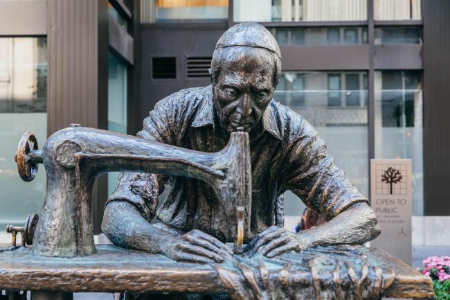 A close view of the Garment Worker statue featuring an older Jewish Man working on a sewing machine