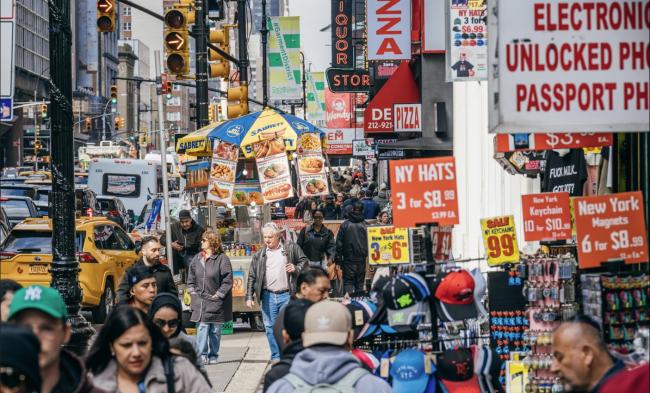 a crowded scene looking north on 8th avenue filled with pedestrians and storefronts
