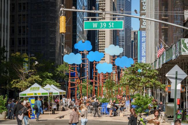A wide view of the opening of Clouds, with lively green plants in the foreground along with white tents and a 39th Ave sign aboce the blue clouds. 