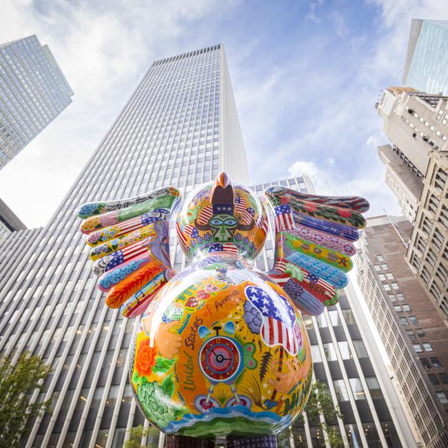 Shot from below of brightly-colored bird sculpture with skyscrapers behind it