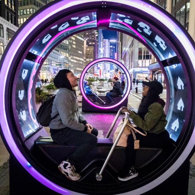 A couple sitting inside a lit-up LOOP sculpture at night