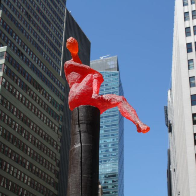 Red figure atop a black post with skyscrapers in the background