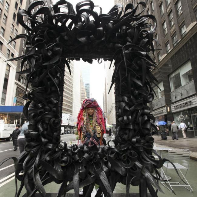 Sculpture made from recycled materials frames the artist who is standing behind it.