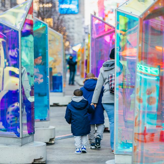 A woman and two children walking between two rows of glass prism sculptures
