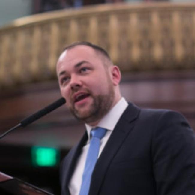 Speaker Corey Johnson speaking into a mic in city council chambers.