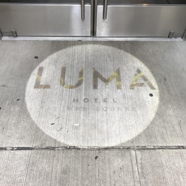 The Logo of the LUMA hotel  on the sidewalk outside of the entrance