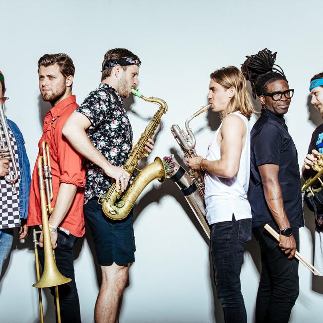 A colorfully dressed group of musicians holding mostly brass instruments.